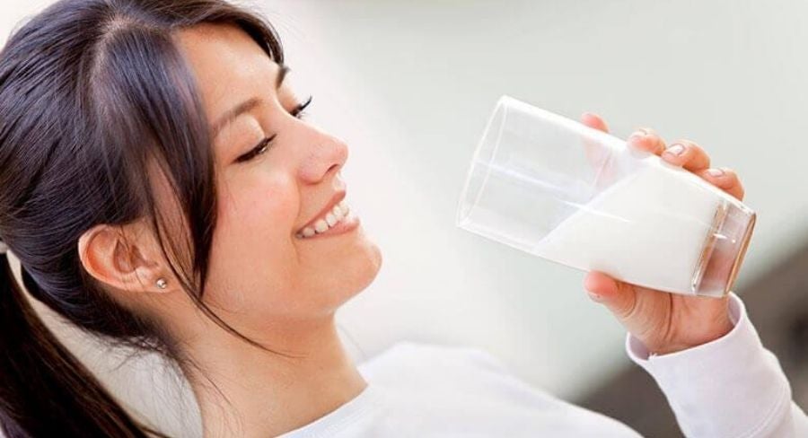Mujer  feliz tomando leche pasteurizada en casa con vaso transparente