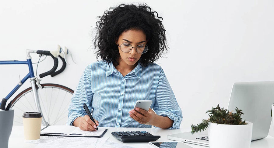 mujer pensativa haciendo cálculos con su celular y tomando notas