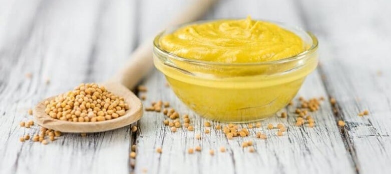 Cuchara de palo con semillas de mostaza y recipiente de vidrio con salsa de mostaza